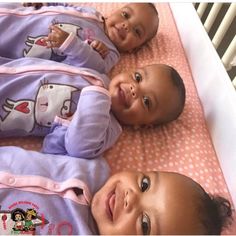 three babies laying in a crib smiling at the camera