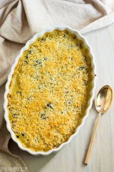 a casserole dish with cheese and spinach in it next to a spoon