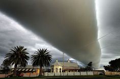 a large cloud is in the sky over a house and palm trees on a cloudy day