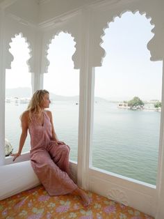 a woman sitting on top of a window sill looking out at the water below