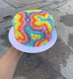 a hand holding a colorful cake on top of a white plate