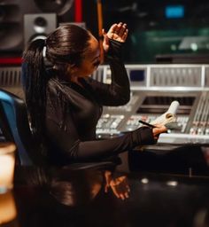 a woman sitting at a desk in front of a sound mixing console holding her hand up to her ear