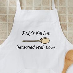 a white apron that says lady's kitchen seasoned with love and a wooden spoon