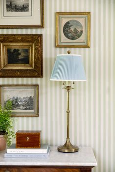 a lamp sitting on top of a white table next to pictures and a potted plant