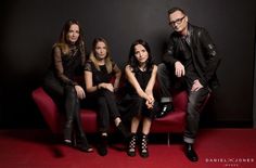 a group of people sitting on top of a red couch next to each other in front of a black wall