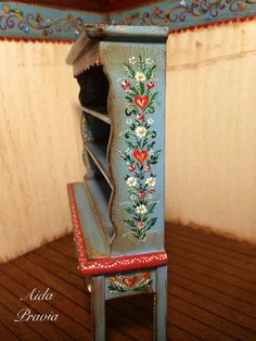 a miniature painted wooden chair with flowers and hearts on the seat, in front of a wood paneled wall