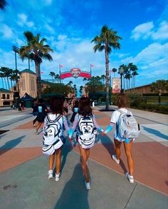 two girls in cheerleader outfits walking down the street with backpacks on their backs