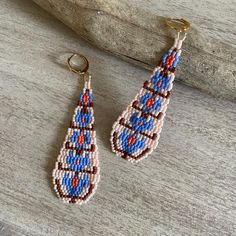 two beaded earrings hanging from hooks on a piece of driftwood, one is blue and the other is red