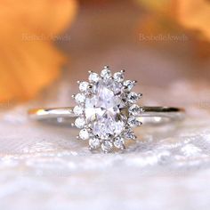 a close up view of a diamond ring on a white lace surface with leaves in the background