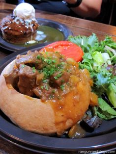 a plate topped with meat and vegetables on top of a wooden table next to another plate