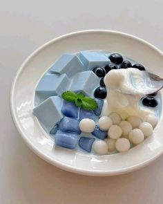 a white plate topped with blueberries and marshmallows next to a spoon