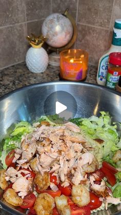 a salad with shrimp and tomatoes in a metal bowl on a kitchen counter next to candles