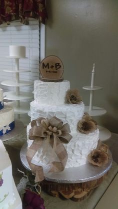 a three tiered white cake with brown bows on the top and bottom, sitting on a table next to other cakes