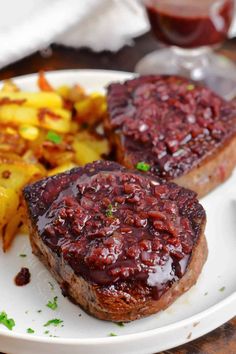 two pieces of steak covered in red sauce on a plate with potatoes