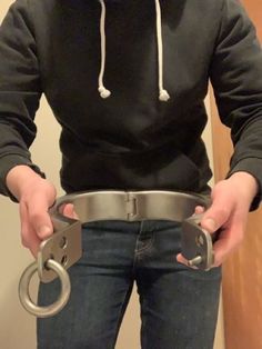 the man is holding two metal handcuffs in his hands while wearing a black hoodie