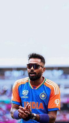 a man with sunglasses on standing in front of a soccer field wearing an orange and blue uniform