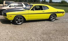 a yellow and black muscle car parked in a parking lot next to other cars on gravel