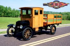 an old model truck is driving down the road in front of some trees and grass