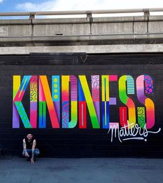 a man sitting on the ground in front of a wall that has been painted with colorful letters