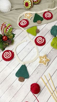 crocheted christmas ornaments and knitting needles laid out on a white wooden surface with yarn