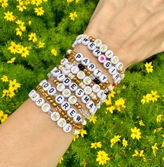 a woman's arm with several bracelets on it and yellow flowers in the background