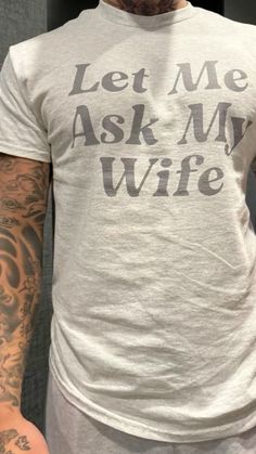 a man with tattoos wearing a white t - shirt that says let me ask my wife