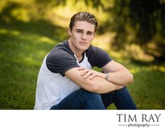 a young man sitting in the grass with his arms crossed