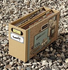 an open file box sitting on top of some rocks and gravel next to a pile of papers