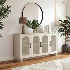 a living room with a white cabinet and mirror on the wall next to a potted plant