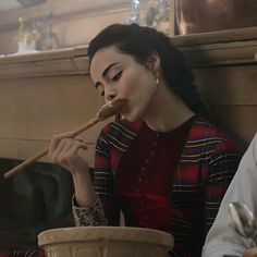 a woman sitting down eating food from a bowl with chopsticks in her mouth