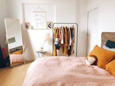 an unmade bed in a bedroom with orange pillows and clothes hanging on the rack