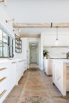 a long kitchen with white cabinets and wooden beams on the ceiling, along with an area rug