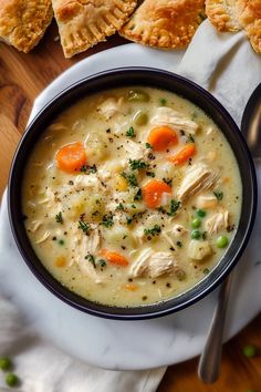 a bowl of chicken pot pie soup on a white plate next to two pieces of bread