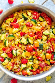 a pot filled with corn and vegetables on top of a table next to spoons