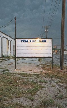 a sign that reads pray for rain in front of an empty building with no doors