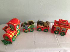 a table topped with red and green toy train cars next to each other on top of a white cloth covered table