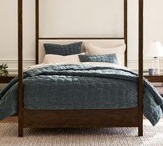 a four poster bed with blue quilts and pillows in a white walled bedroom area