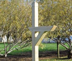 a wooden cross sitting in the middle of a field next to some trees and grass