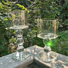 two clear glass goblets sitting on top of a wooden table in the woods