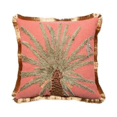 a pink and gold pillow with a palm tree on the front, fringe trim around the edges