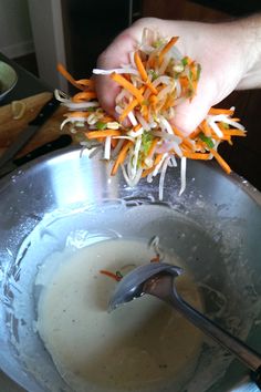 someone is adding shredded carrots to the soup in a large silver bowl with a spoon