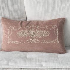 a white couch with a pink pillow on it's back and an embroidered border