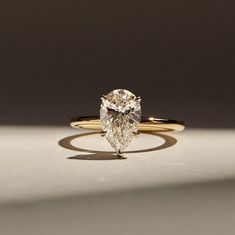 a yellow gold ring with a pear shaped diamond in the center, on a white surface