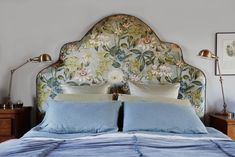 a bed with blue sheets and pillows in a bedroom next to two bedside lamps on either side of the headboard