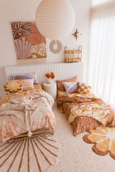 two beds with colorful comforters and pillows in a white room next to a window