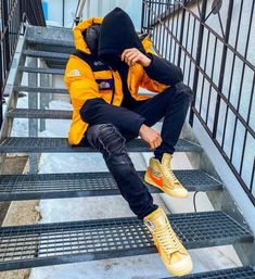 a man sitting on some stairs wearing yellow sneakers and a jacket with the hood up