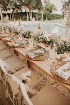 a long table set up with place settings for dinner next to a swimming pool in the background