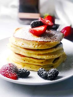 a stack of pancakes topped with berries and powdered sugar on a white plate next to some strawberries