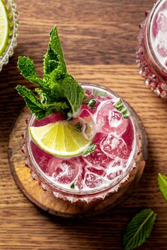 two glasses filled with different types of drinks on top of a wooden table next to limes and mint