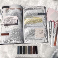 an open book sitting on top of a white blanket next to markers and pencils